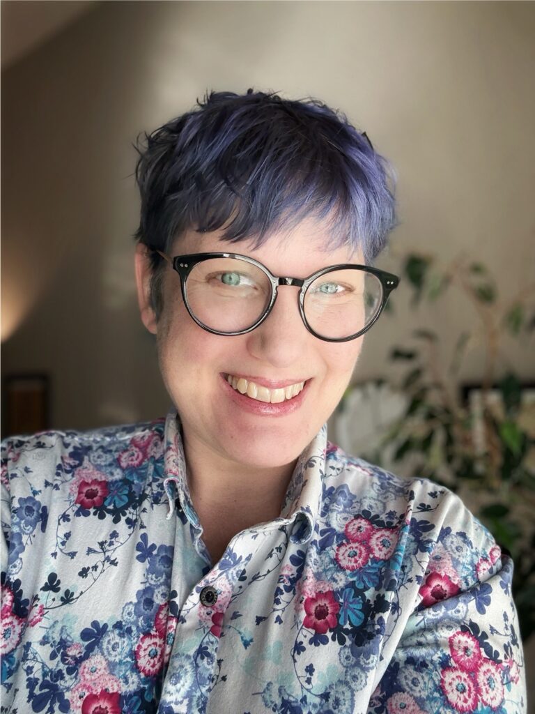 A portrait photograph of a white woman with short purple hair and glasses